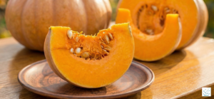 Un dovleac plăcintar întreg și felii proaspete cu miez portocaliu intens și semințe, așezate pe o masă de lemn în lumină naturală.