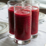 Trei pahare înalte, cilindrice, pline cu un smoothie dens de culoare roșu-purpuriu intens, așezate pe o masă cu față de masă albă și veselă elegantă.