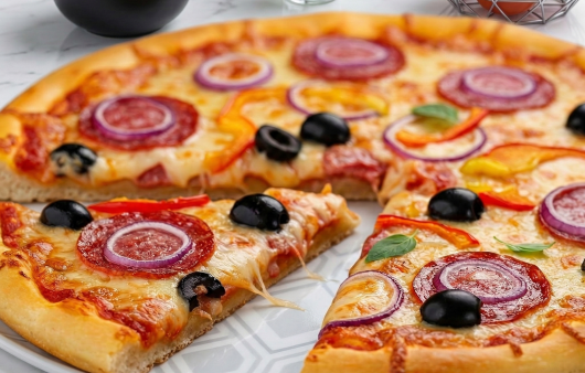 O pizza de casă abia scoasă din cuptor, așezată pe un platou decorat, cu topping generos de salam, rondele de ceapă roșie, măsline negre și ardei, alături de sos de roșii și ingrediente proaspete.