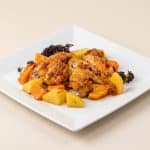O farfurie albă pătrată cu aripioare de pui rumenite, acoperite cu o crustă de parmezan, servite alături de bucăți de cartofi, morcovi și broccoli la cuptor, pe un fundal crem deschis.